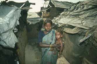 INDIA, Delhi, Woman holding small child in slum housing area