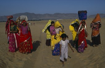 INDIA, Rajasthan, Pushkar, Brightly dressed Rajasthani women and children carrying loads on their