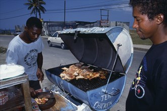 WEST INDIES, Jamaica, Market, Man cooking jerk chicken on roadside stall with waiting customer.