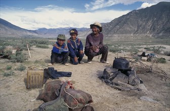 CHINA, Tibet, Jiang, Shepherd and family crouching by camp in open landscape