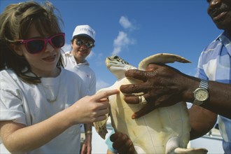 WEST INDIES, Cayman Islands, Grand Cayman, Young girl touching turtle held by man in the Turtle