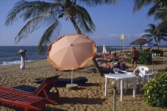SRI LANKA, Negombo, Sandy beach with umbrella shading tourists lying on sunbeds and a shell vendor