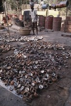 INDIA, Goa, Colva, Copra worker with piles of coconut shells in the foreground and oil drums behind