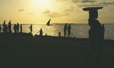 TANZANIA , Zanzibar, Zanzibar, People on the waterfront silhouetted against yellow sunset with dhow