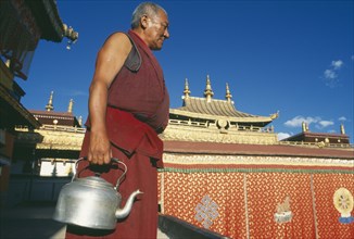 TIBET, Lhasa, Jokhang Temple, Monk carrying kettle on the roof of the temple