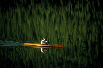USA, Montana, Salmon Lake, Single canoeist on lake with reflection of trees in the water near
