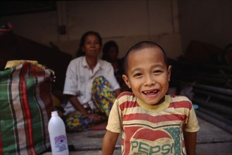 THAILAND, North, Mae Sai , Karen refugee boy smiling in foreground with mother in the background