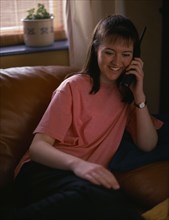 COMMUNICATIONS, Phones, Smiling teenage girl sat on sofa using cordless telephone Model Released