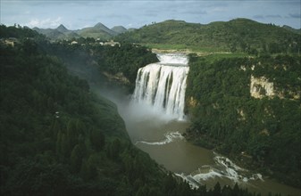 CHINA, Guizhou, Huangguoshu Falls seen from a distance within lush green surrounding landscape