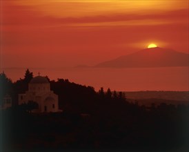 GREECE, Dodecanese Islands, Kos, "View past domed church in rural landscape to sun setting behind