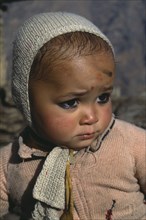 INDIA, Uttar Pradesh, Himalayan baby looking unhappy.  Black kohl ringed eyes and mark on forehead