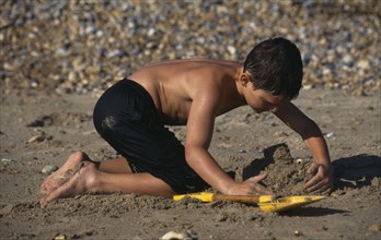 CHILDREN, Playing, Beach, Boy on pebbly & sandy beach making a sand castle