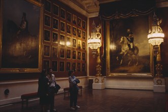 RUSSIA, St Petersburg, "The Hermitage Museum interior, room hung with portaits, three people look