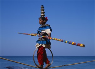 INDIA, Goa , General, "Young girl walks the tightrope while balancing silver pots on her head, blue