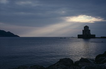 GREECE, Peloponnese, Methoni, View across the sea towards fortress ruins lit by evening sun rays