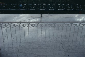 GREECE, Reflection, Decorative wrought iron balcony railings casting a shadow onto a pale wet floor