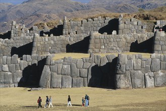 PERU, Cusco Department, Sacsayhuamán, People walking infront of the Inca walls.