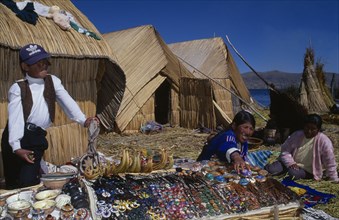 PERU, Puno, Lake Titicaca, Uros women and young boy selling sounvenirs outside reed houses on a