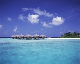 MALDIVES, Baros, "View across expanse of turquoise sea towards thatched beach huts on stilts, beach