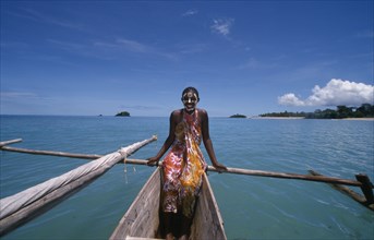 MADAGASCAR, Nosy Be, Young girl on a pirogue canoe wearing a colourful sarong and with her face