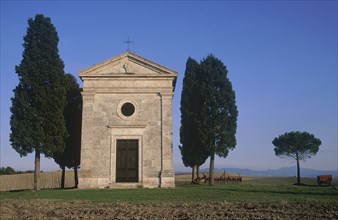 ITALY, Tuscany, San Querico, "Small stone chapel, facade with cypress trees growing beside it in an