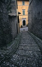 ITALY, Umbria, Spoleto, A narrow cobbled street leading down towards a yellow painted building