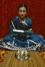 SOCIETY, Religion, Hinduism, England.  Girl reading Holy book in front of lighted candles and