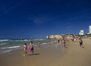 PORTUGAL, Algarve, Praia da Rocha, View along beach with people walking along the waters edge