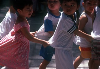 VIETNAM, Hanoi, "Group of young children, holding on to each other’s clothing to form a line. "