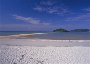 MALAYSIA, Langkawi, Kedah, Pantai Cenang beach with man walking near the the sand bar at low tide