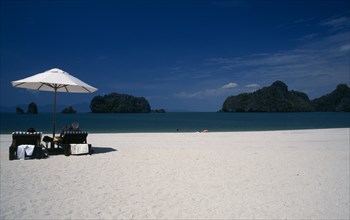 MALAYSIA, Kedah, Langkawi, Pantai Rhu beach with tourists sitting under an umbrella looking out to