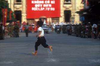 VIETNAM, Boy, "Young boy running across a road, soldiers just seen in the distance behind."