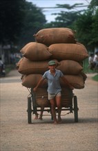 VIETNAM, Transport, Man pulling a loaded cart stacked high with sacks behind him.