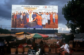 CAMBODIA, Phnom Pehn, Election poster with line of stalls selling fruit along the roadside in front