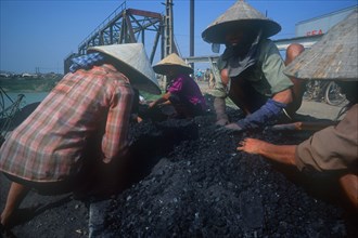 VIETNAM, Bac Giang, Coal ladies crouched on piles of coal wearing traditional conical hats.