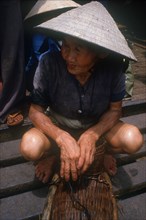 VIETNAM, Quang Binh Province, Dong Hoi, Old woman in a conical straw hat crouched on ferry deck.