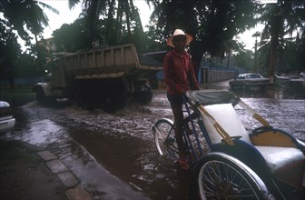 CAMBODIA, Phnom Pehn, Rickshaw and truck driving through a flooded street near the Royal Hotel