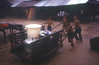 CAMBODIA, Thmar Pouk, A group of young boys pushing a handcart loaded with large containers in
