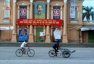 VIETNAM, North, Haiphong, Cyclist and cyclo driver in front of a building draped with commemorative