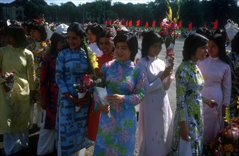 VIETNAM, Hanoi, Young women wearing traditional Cao dai dresses and holding flowers waiting at the