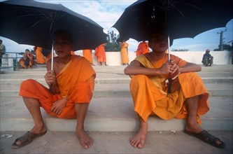 LAOS, Vientianne, Two young monks seated on wide stone steps under umbrellas.