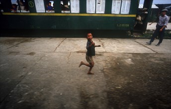 VIETNAM, Vinh, Young boy running along platform of railway station in front of stationary carriage