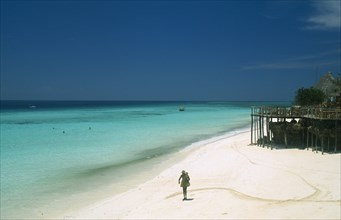 TANZANIA, Zanzibar Island, "Nungwi.  Single figure walking along sandy beach beside aquamarine