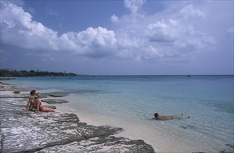 TANZANIA, Zanzibar Island, Mangapwani, Young couple sitting on flat rocks on the shoreline looking