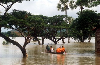 CAMBODIA, East, Two Budhist monks in a canoe being rowed through flood water on Route 1 from Neak