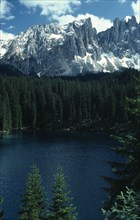 ITALY, Trentino-Alto Adige, Dolomites, Conifer trees lining Lake Carezza below Mount Latemar