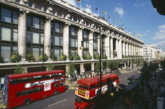 ENGLAND, London, Selfridge’s store exterior with red double decker buses going past on the road in
