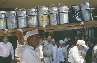 INDIA, Maharashtra, Bombay, A Dhaba Wallah at Victoria terminus carrying many tins on his head