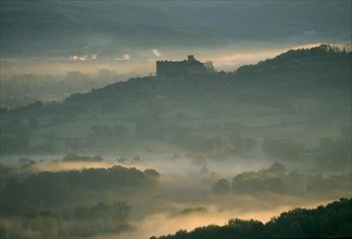 FRANCE, Aquitaine, Dordogne, "Castelnau-Bretenoux Castle silhouetted on hillside against pale,