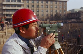 CHINA, Shaanxi Province, Xian, Surveyor using a theodolite working on a building construction site.